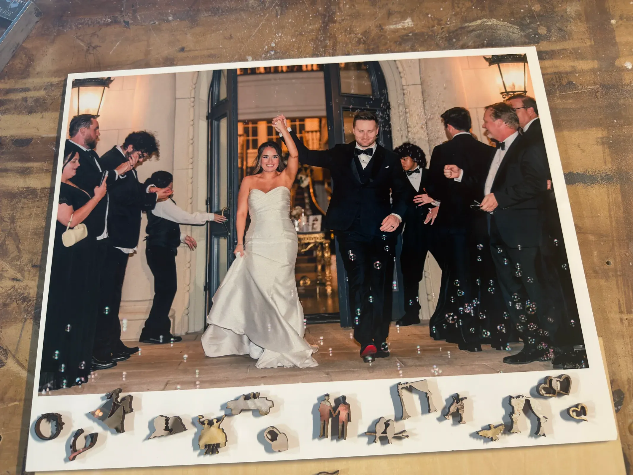 A real wedding photograph on hardwood with personalized wedding-shaped pieces arranged along the edge